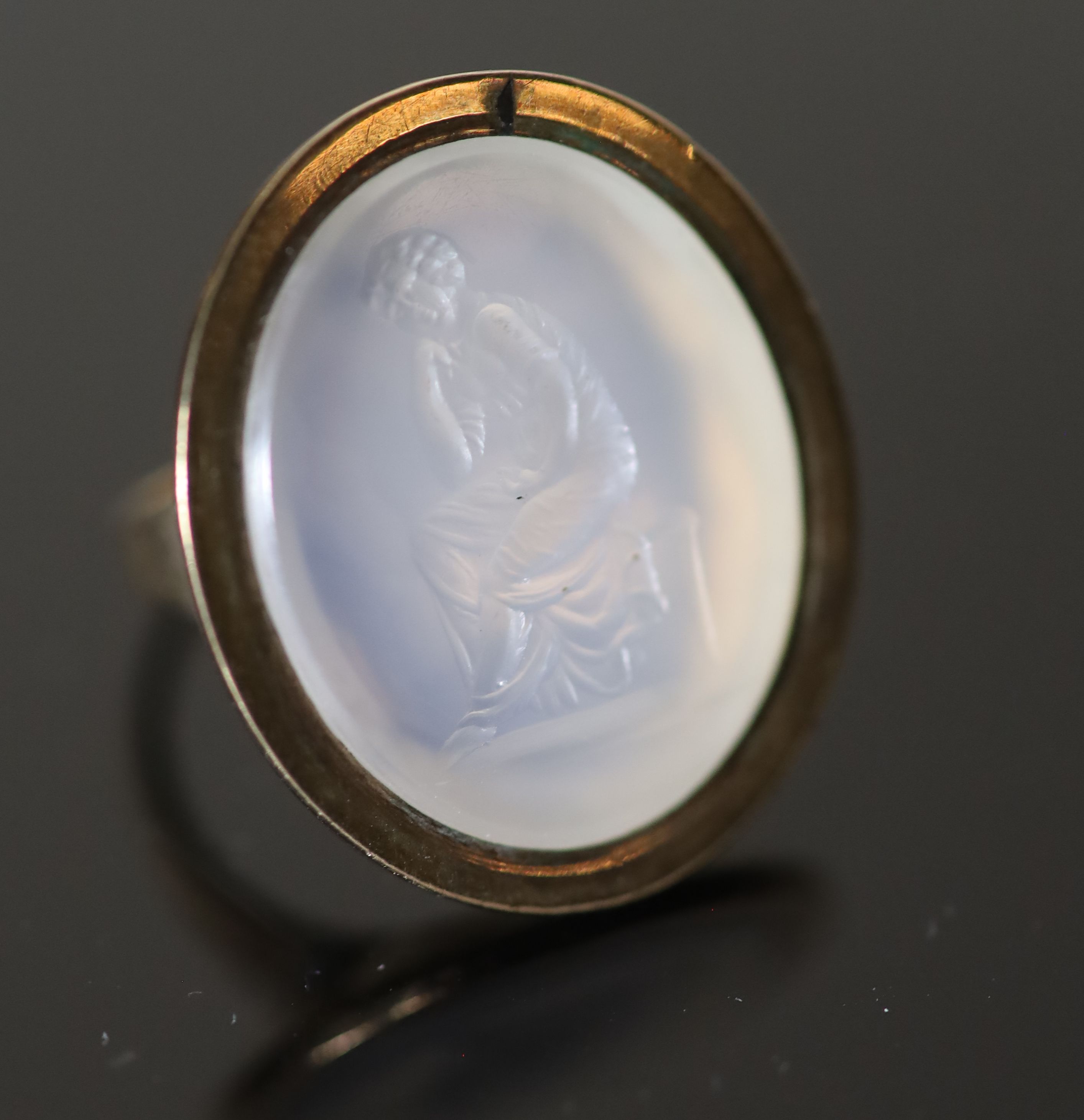 An early 19th century gold and white agate oval intaglio ring, carved with a seated figure,